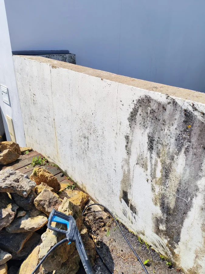 Mur de clôture côté rocaille avec traînées noires, lance du nettoyeur haute pression en place