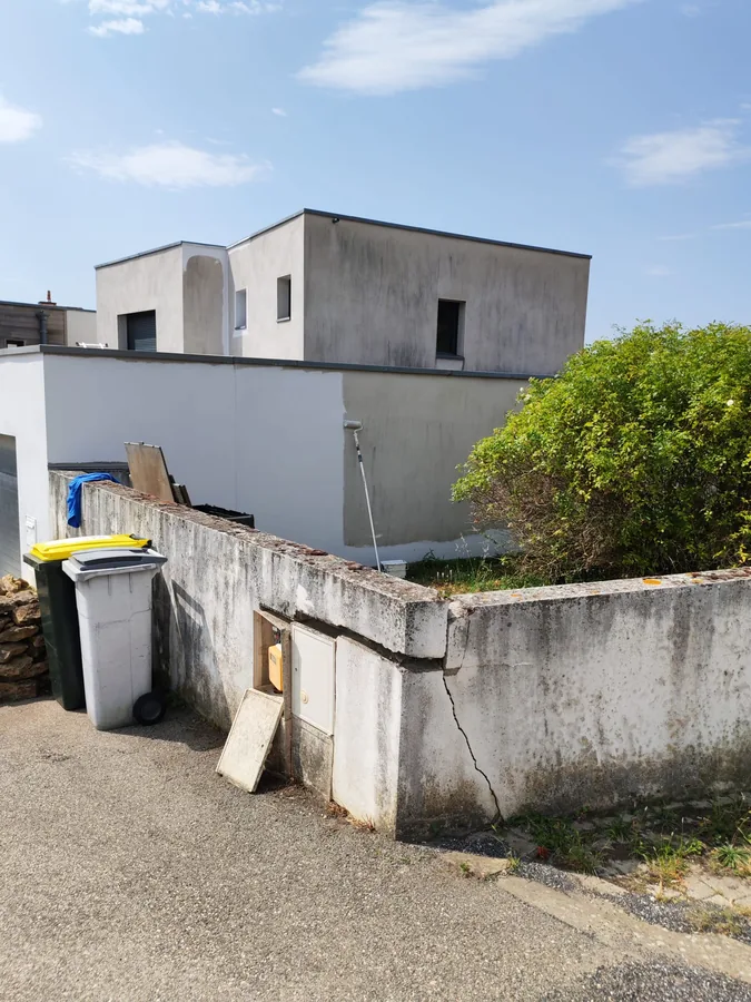 Vue d'ensemble en cours de chantier : mur de clôture fissuré au premier plan, façade en cours de peinture